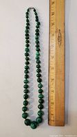 Handmade malachite necklace laid out next to a wooden ruler showing length about 18 inches.