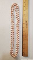 Full length view of double-strand pink baroque pearl necklace alongside a ruler showing it measures approximately 26 inches long.