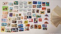Top view of about 60 loose colorful postage stamps arranged on a white surface showing various designs and countries