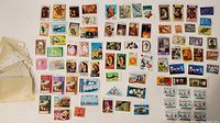 Overview photo showing approximately 80 loose postage stamps from various countries spread out on a white surface.