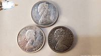 Obverse side of three silver dollar coins showing Queen Elizabeth II portraits with varying designs and inscriptions.