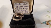 Three sterling silver rings displayed in a black velvet ring box with a handwritten tag indicating they are solid sterling silver with CZ accent stones, marked 925.