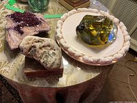 View of amethyst cluster, raw stone, glass piece, and ceramic shell platter arranged on a table.