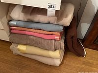Stack of 7 vintage wool blankets in cream, brown, beige, pink, blue, orange and yellow hues, folded and stacked on floor.