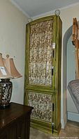 Front view of tall wooden cabinet with green distressed finish and shirred fabric panels on door