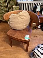 Front view of chair with curved backrest and beige pillow on wooden floor.