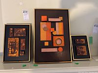 Three framed sculptures displayed side by side on a shelf