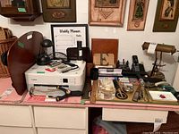 Wide view of desk surface showing Canon printer, leather organizer, weekly planner, multiple staplers, bell, scissors, rulers and other small office items arranged over desk.