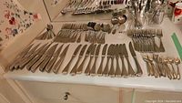 Overview of arranged flatware on surface showing knives, forks, spoons and cutters in stainless silverplate finish with various designs.