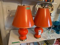 Two orange ceramic table lamps with shades on tabletop