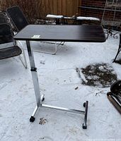 Full view of over bed table showing metal frame with composite wood grain top and caster wheels.