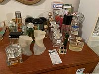 Full view of assorted perfume bottles arranged on wooden surface including Gucci bottle, frosted textured bottles, clear glass bottles, and a glass bowl with soaps in background.