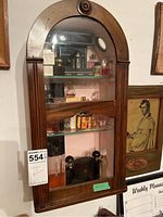 Frontal view of arched-top wood cabinet mounted on wall showing three shelves filled with various perfume bottles