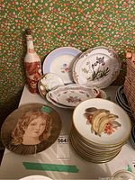 Main overview of the lot showing stacked fruit plates with banana design, decorative floral plates, and a decorative bottle