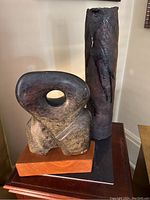 Stone sculpture on cherry wood base and dark ceramic vase on black metal tile, overall view