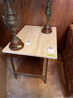 Front and top view showing light stone surface with natural veining, rectangular shape, gold-tone metal legs, and wooden shelf below.
