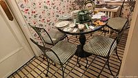 Full set of round cast iron pedestal table with glass top surrounded by five matching chairs with gingham cushions, dishes on top not included