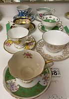 Seven vintage teacups and saucers arranged on a white table