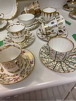 Six teacup and saucer pairs in various hand decorated gilt and colored leaf patterns displayed together