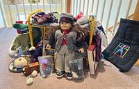Front view of American Girl Samantha doll standing in front of yellow metal bunk bed with folded clothes and accessories spread around, including books and wooden snowman chair.
