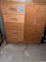 Front view of wooden childrens wardrobe showing five drawers with wooden handles on left, single cabinet door on right, mounted on castors. Surface scratches visible.