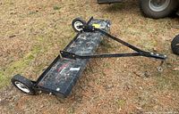 Full side view of the Brinly dethatcher showing the black metal frame, two wheels, and attachment arm with rust spots.