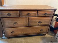 Front view of wood dresser showing all five drawers with metal handles and visible wear.