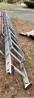 Full view of aluminum extension ladder with roof stabilizer laid on grass showing length and condition.