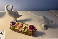 Photo showing two matte finish Lladro geese figurines and Thorley floral bone china log on a white surface