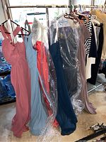 Six long evening gowns hanging on rack in garage, various colors and some in garment bags
