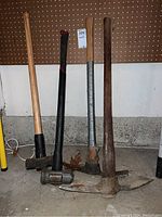 Full view of two picks and two mallets leaning against pegboard with concrete wall background.