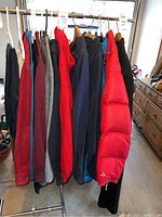Photo of men's jackets, coats, sweaters, and sweatshirts hanging on a clothing rack with one bright red puffer coat