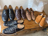 Five pairs of men’s shoes arranged on a wooden chest showing black, brown, and tan color shoes with signs of wear.