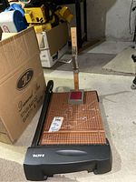 X-Acto paper cutter with brown grid cutting mat and pant hemmer box in basement area.