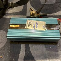 Top-down photo of the PowerBright power inverter showing the exterior casing, a product label with model number, and battery clamp connections on the cord.