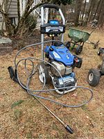Front and side view of the Yamaha Powerstroke power washer on grass, showing hose coiled over the frame and spray wand attached.