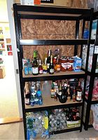 Full frontal view of black metal shelving unit with four pressed wood board shelves, loaded with assorted beverage bottles and cans (not included in the lot). Shows shelving size and construction.
