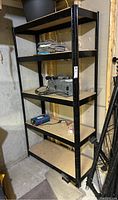 Full view of the shelving unit showing its height and particle board shelves, with some tools and items on shelves (not included).