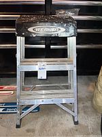 Full view of the Werner folding aluminum stepladder showing the entire ladder with three steps and rubber feet.