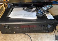 Denon AVR-1705 stereo receiver with Sony BDP-BX2 Blu-ray player and components on top including remotes and papers.