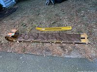 Wooden toboggan lying flat on ground with attached padded cushion and yellow Snurfer beside it.