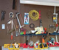 Wall pegboard with hand tools including saws, hammers, pliers, caulking gun, extension cord, and small bins with fasteners.