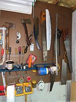 Photo of pegboard with hand axes, hand saws, screwdrivers, rolls of tape, spools of string, and bins of screws and small hardware