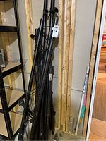 Photo showing black metal tubular truss sections leaning against a wall, assembled from multiple pieces with clamps and brackets visible, showing wear and scratches.