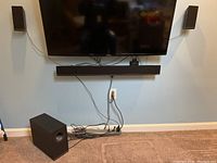 Speakers, sound bar, and subwoofer set installed and placed on carpeted floor below a wall-mounted TV.