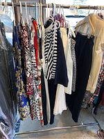 Photo of assorted women's dresses, skirts, tops, shorts, and pajamas hanging on a metal rack in a garage.