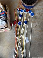 Collection of red and blue reflective yard stakes and yardsticks laid on concrete floor next to potted plant and box