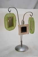 Full view showing the steel tree structure with three hanging glass picture frames in green and beige colors.