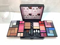 Open compact makeup set showing central bronzer, blush, lip colors, eyeshadow palettes with multiple shades, and small applicators.