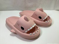 Pink shark slippers showing fun design with shark teeth, eyes, fin and soft sole, viewed from the side